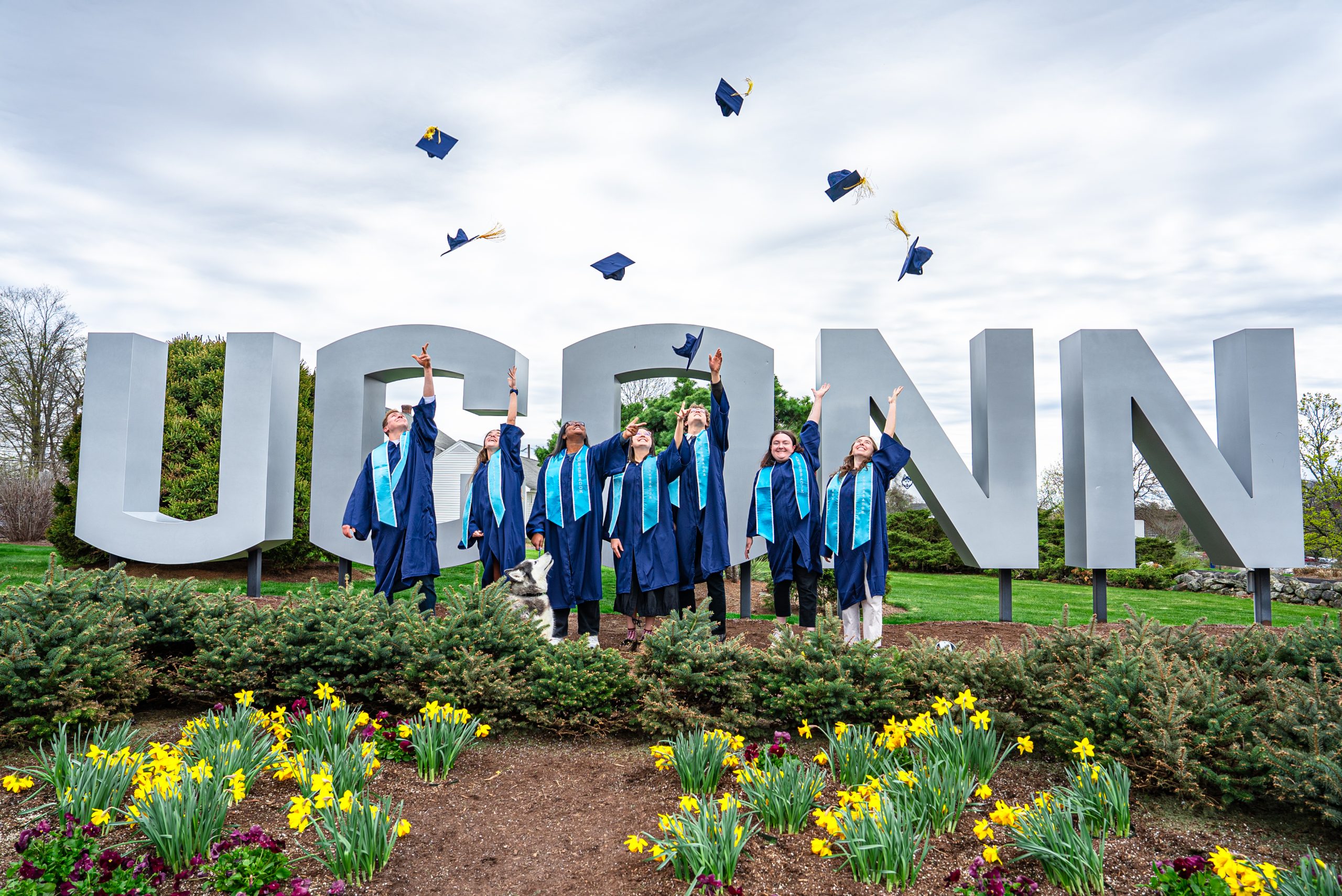 graduates throwing caps in front of UConn sign